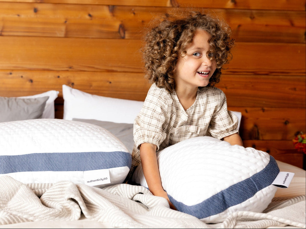 Girl sitting in bed hugging her A50 Travel Pillow.