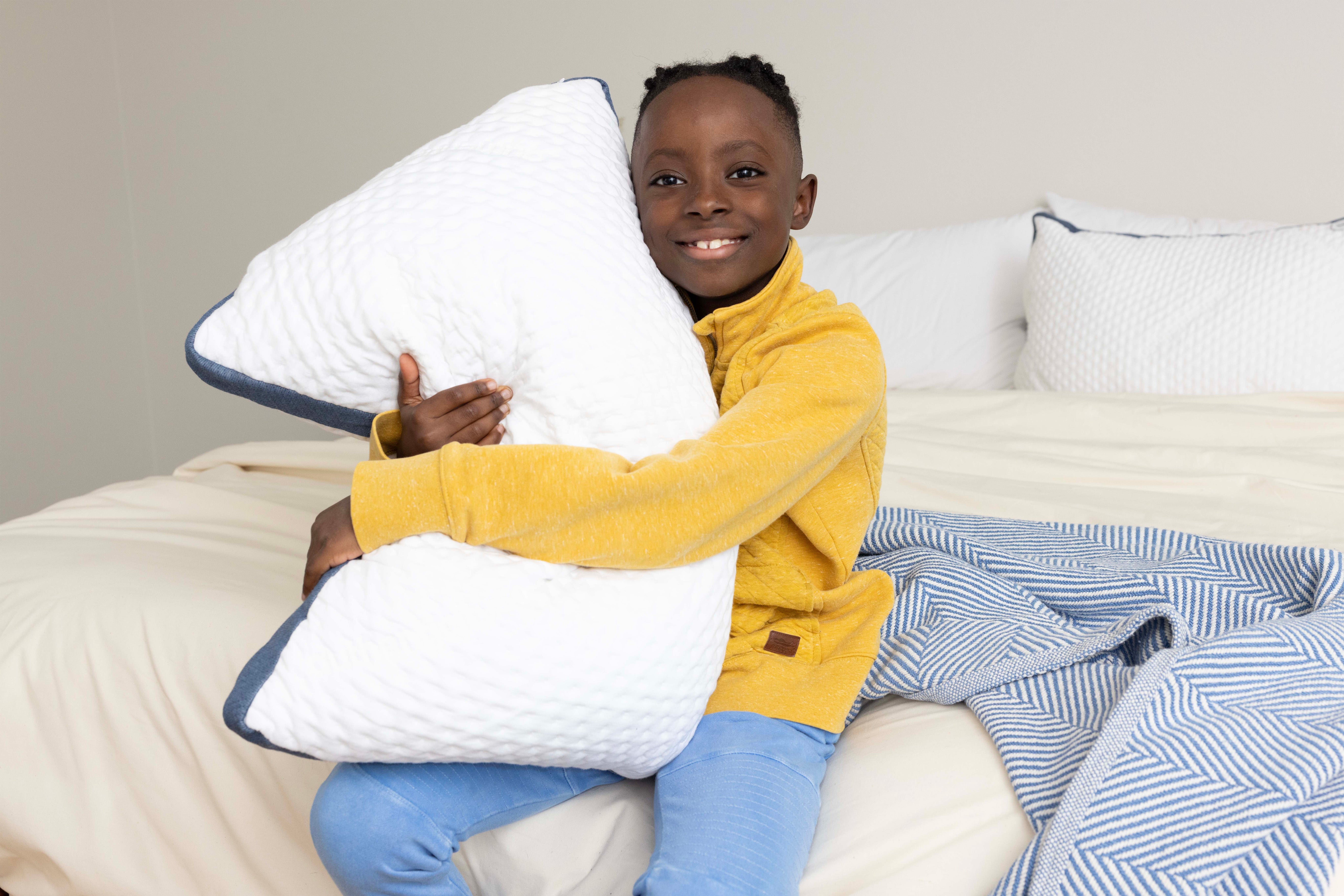Boy sitting on the edge of his bed hugging his Custom Comfort Pillow.