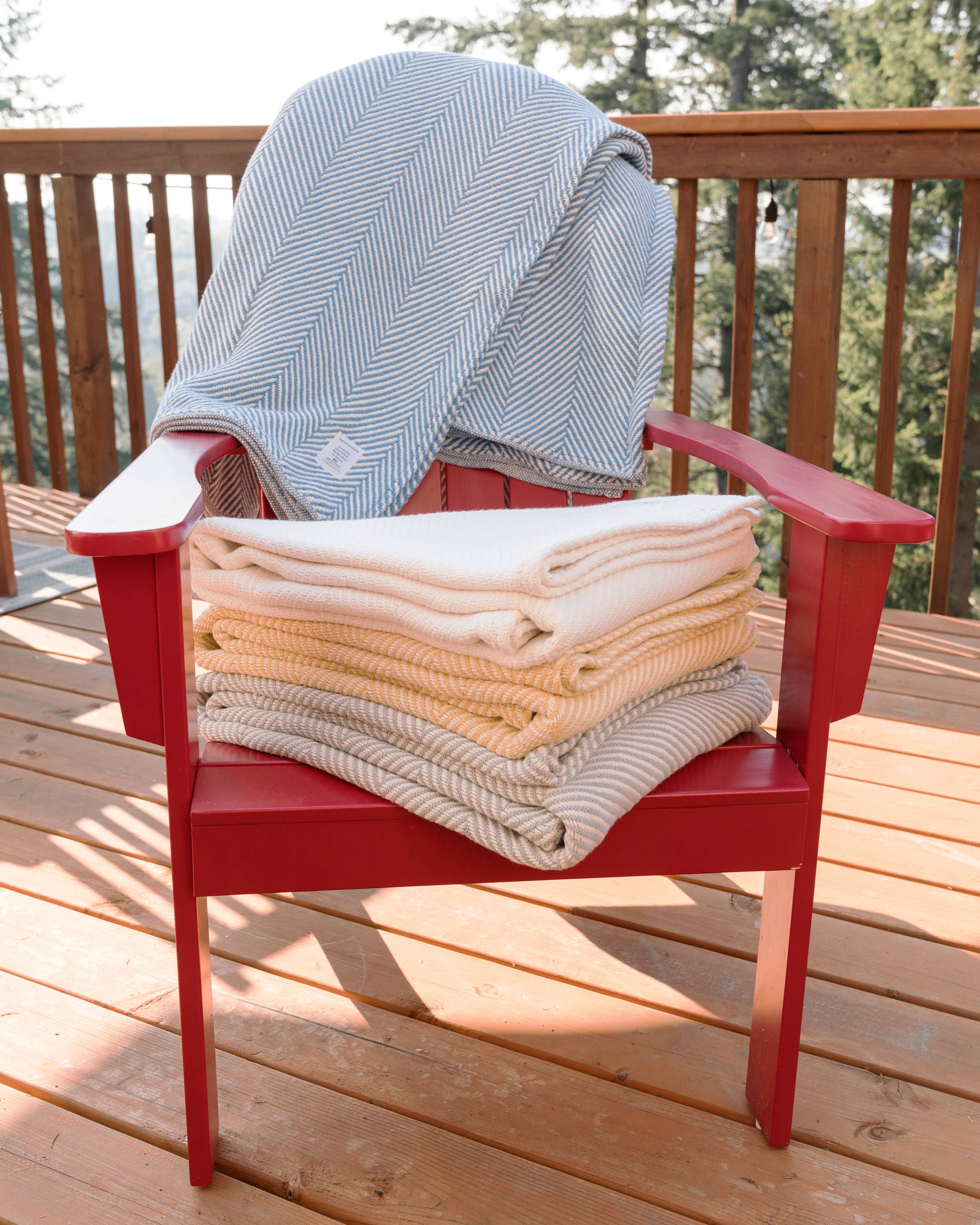 Stack of folded Heritage Blankets on a red chair on a back deck.