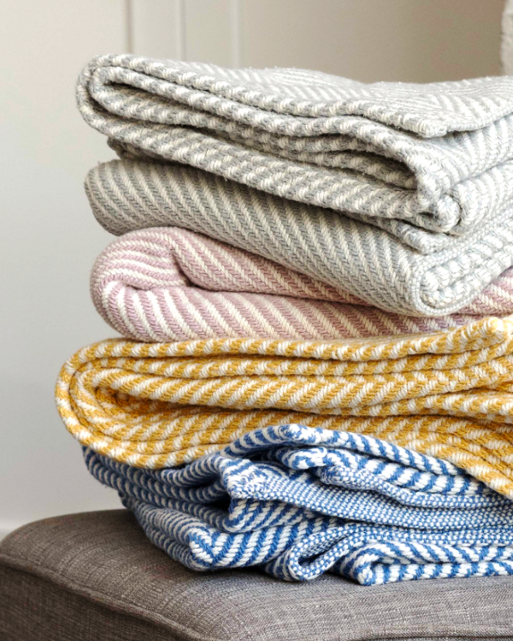 Stack of folded Heritage Blanket throws (in Cascade Gray, Desert Blush, Prairie Yellow, and Coastal Blue.).