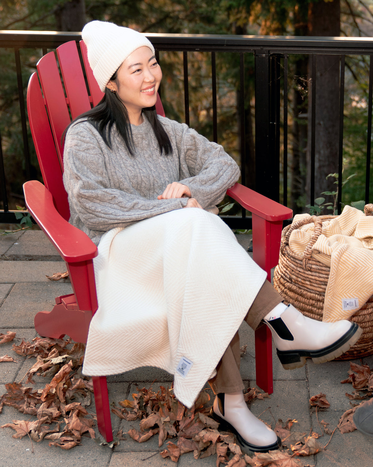 Woman sitting on her back deck in a patio chair with her Island Sand Heritage Blanket.