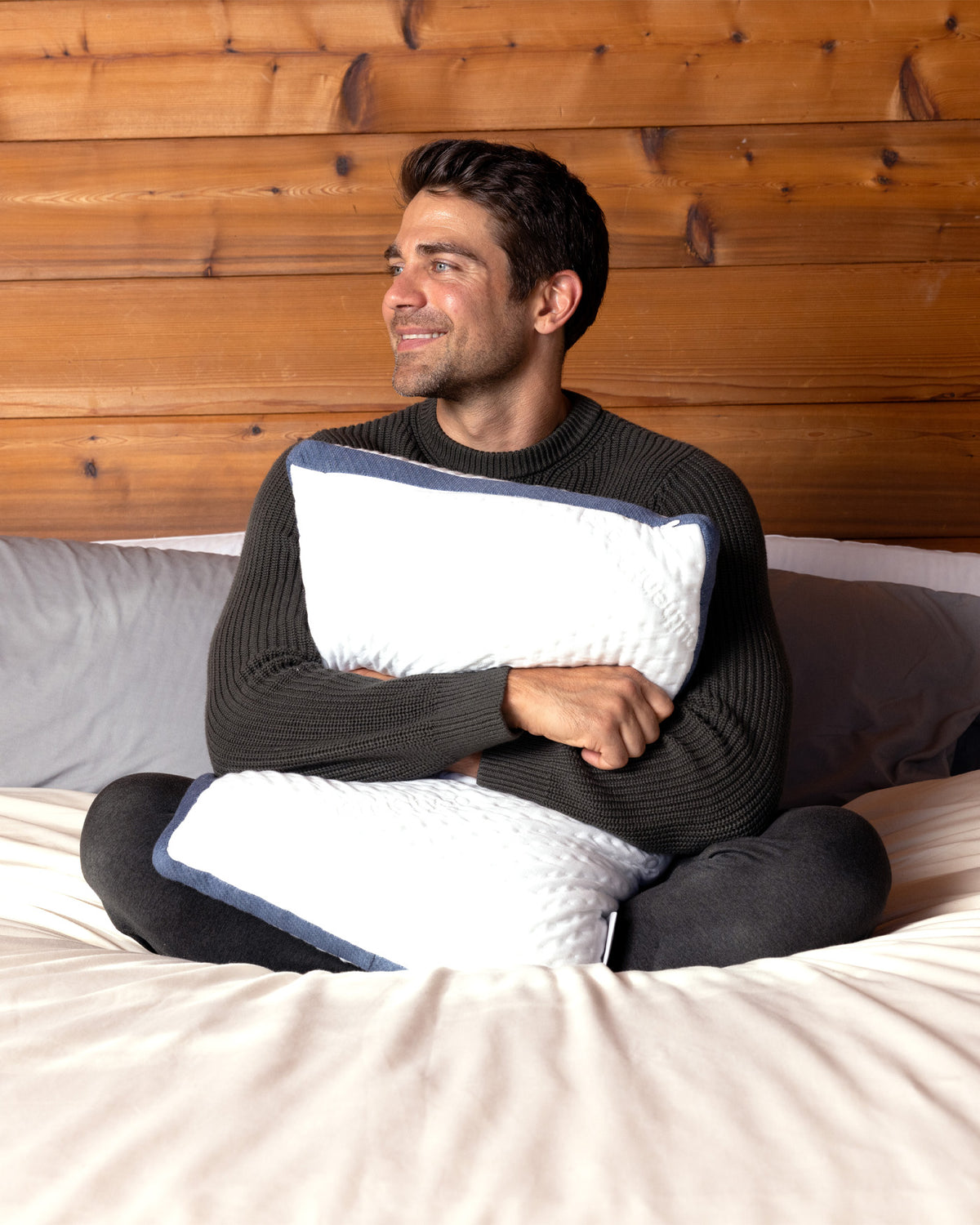 Man sitting in bed, smiling and hugging a Custom Comfort Pillow.