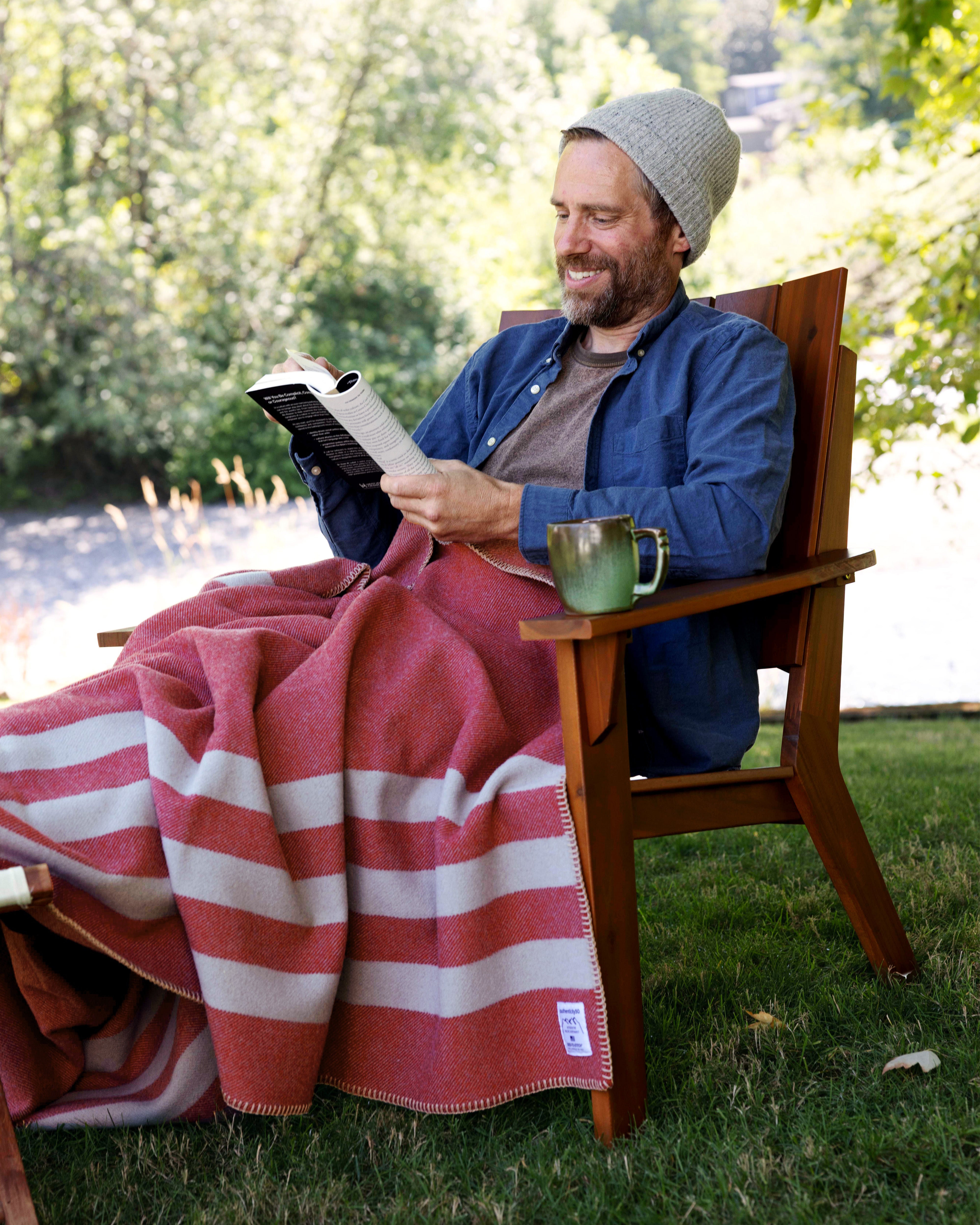 Man sitting in his backyard reading with a Northwest Wool Throw on his lap.