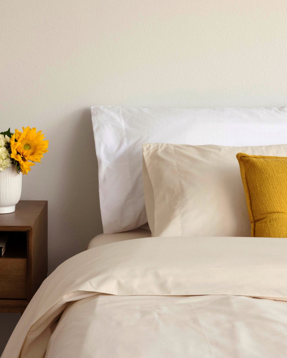 A bed styled with yellow flowers, throw pillows, and Authenticity50's Made in USA cotton bedding.