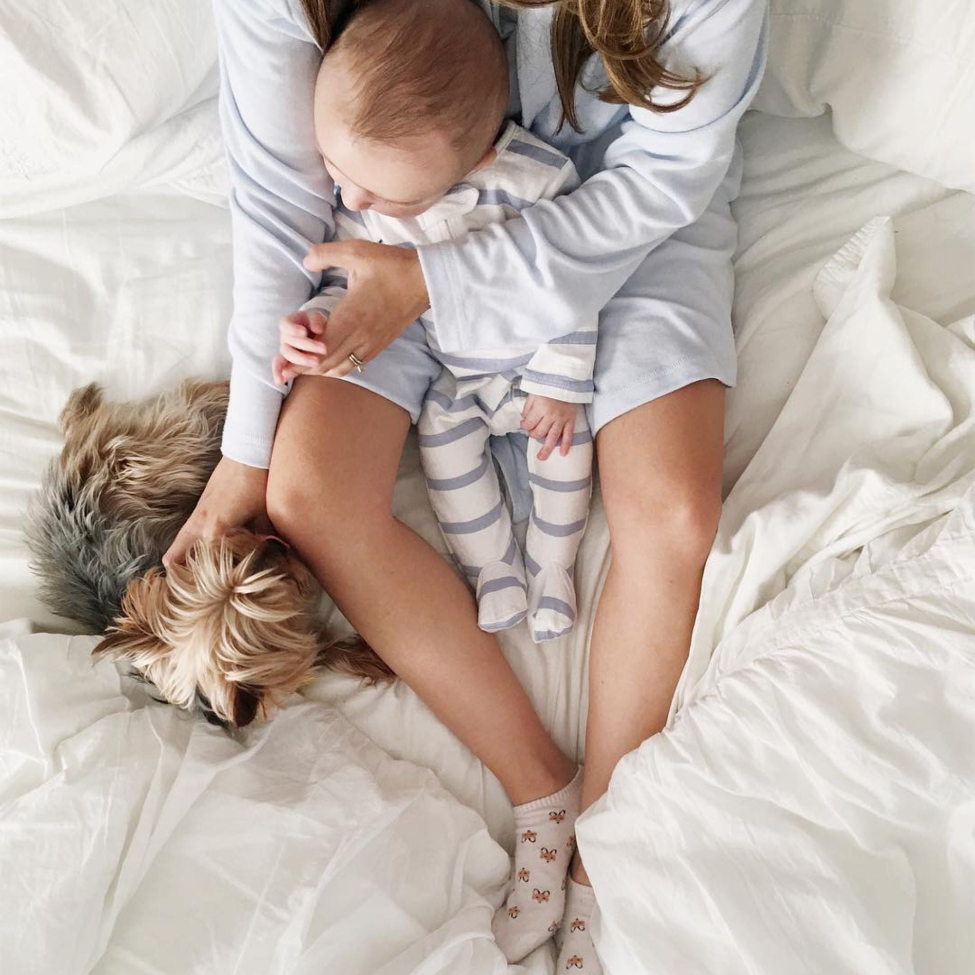 a lady sitting with her child and dog on american made bed sheets 