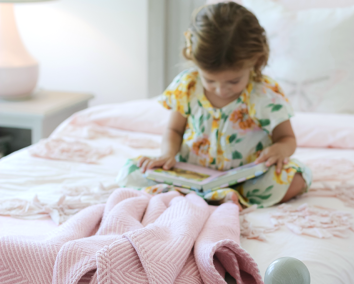Girls sitting in bed snuggled under a Heritage Blanket reading a book.