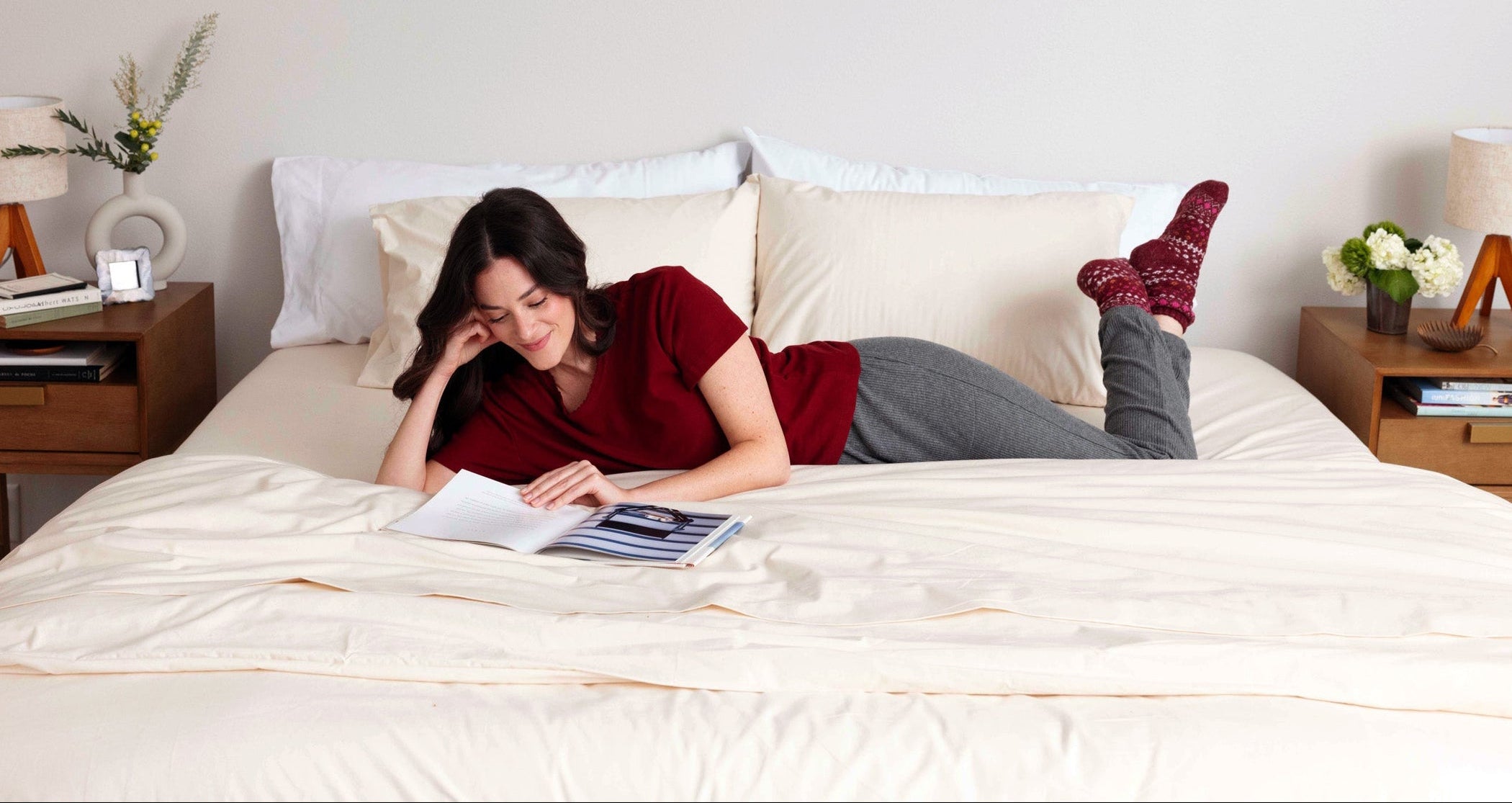 Woman reading and laying in a bed made with Heritage American Sheets. 