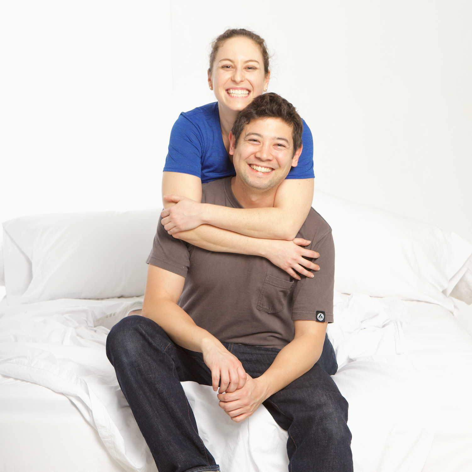 Authenticity50 co-founders Jimmy and Steph sitting on their very own made in usa signature bed sheets made using the very best american grown cotton