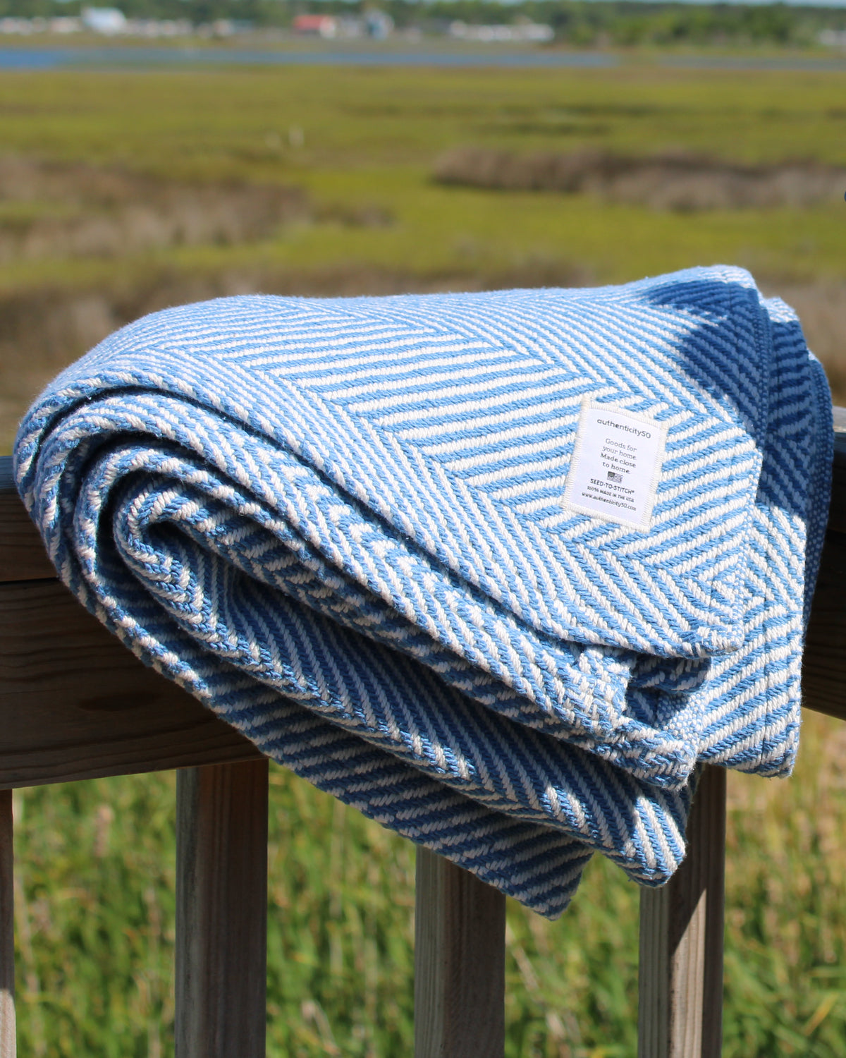 Coastal Blue Heritage Blanket folded and draped over a back deck railing to show off the handstitched tag.