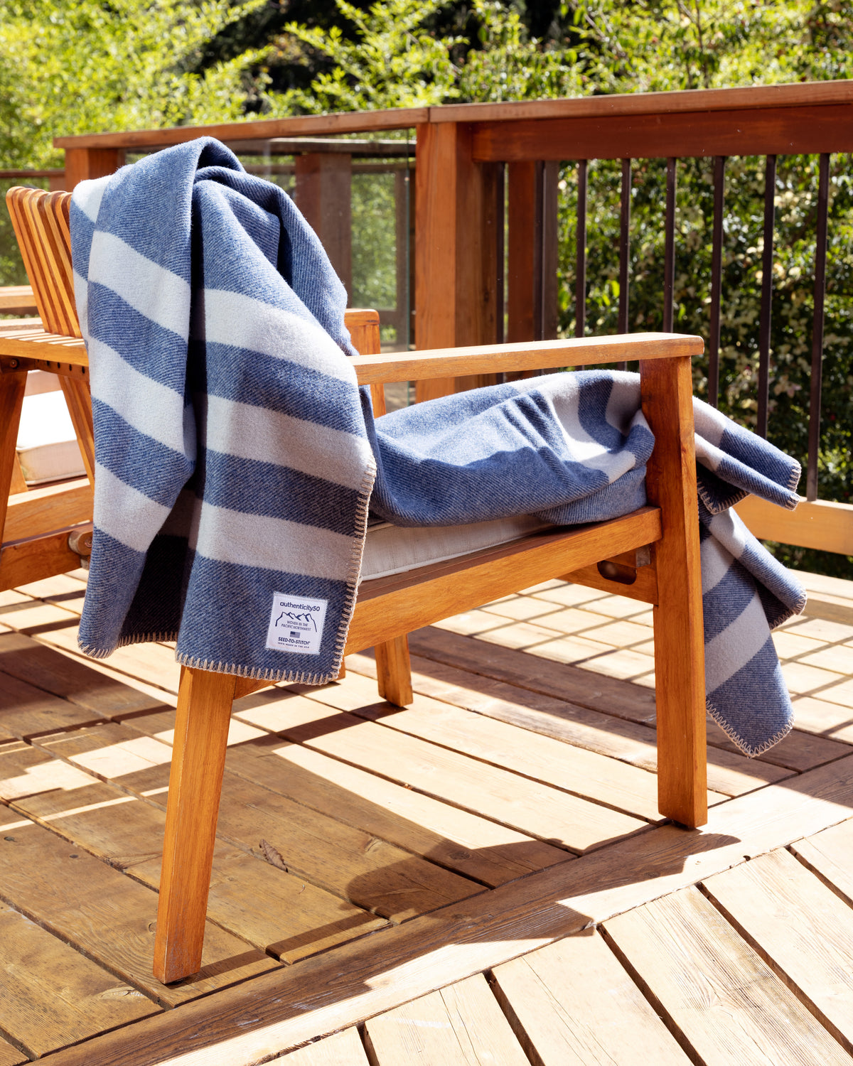 Denim Blue Northwest Wool Throw gently draped on the back of a wooden deck chair.