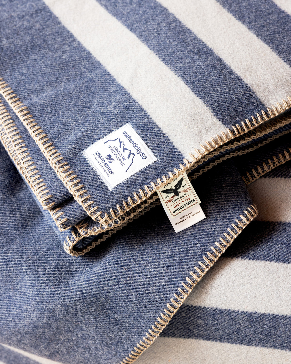 Folded stack of Denim Blue Northwest Wool Throws with the custom-woven Authenticity50 and Pendleton Wool Mills® Made in the United States tags front and center.