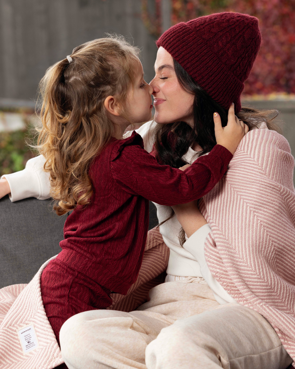 Mother and daughter touching noses and sitting in their backyard with a Heritage Blanket on their laps and shoulders.