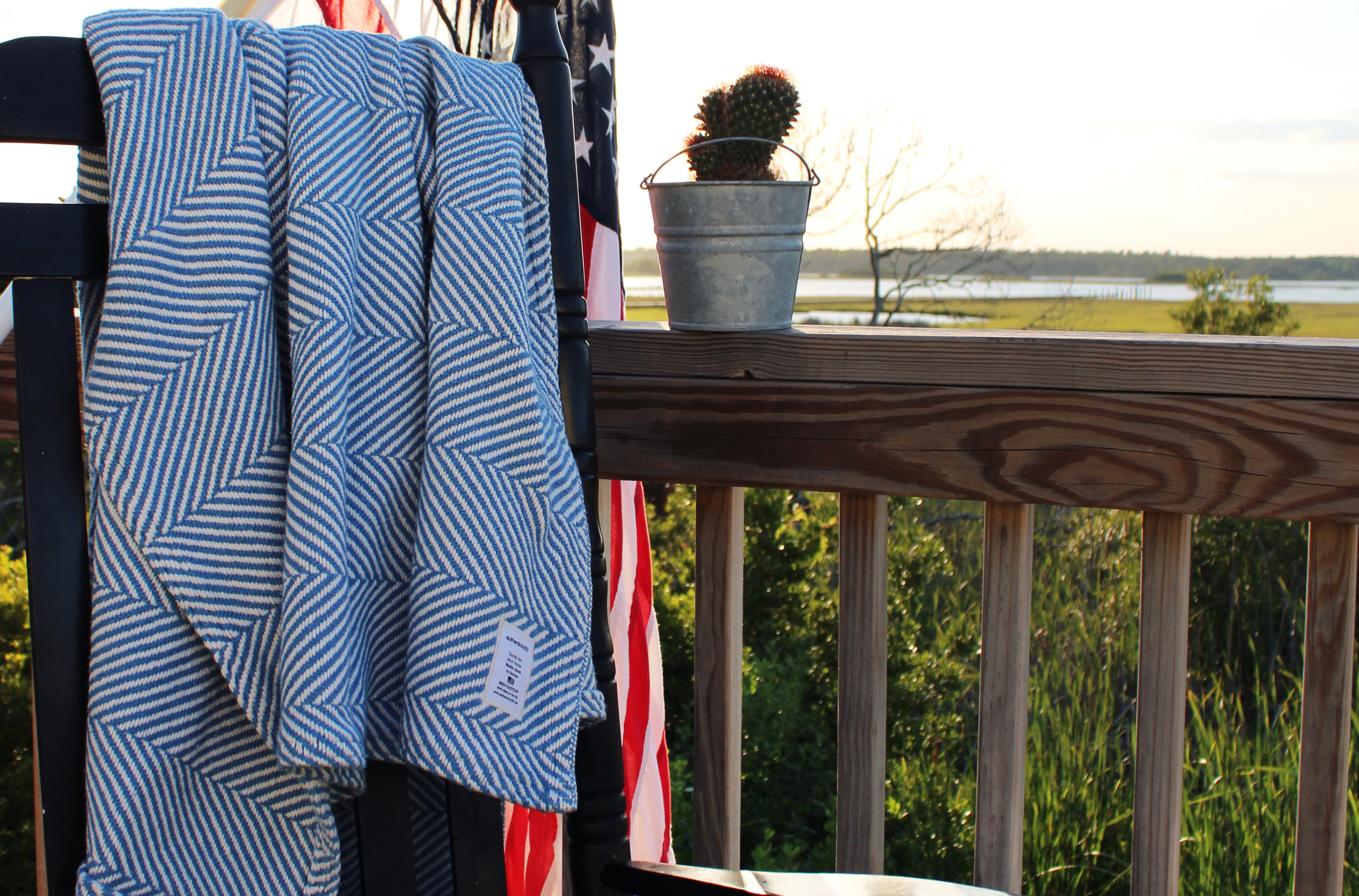 Coastal Blue Heritage Blanket draped on the back of a rocking chair with an American flag hanging in the background.