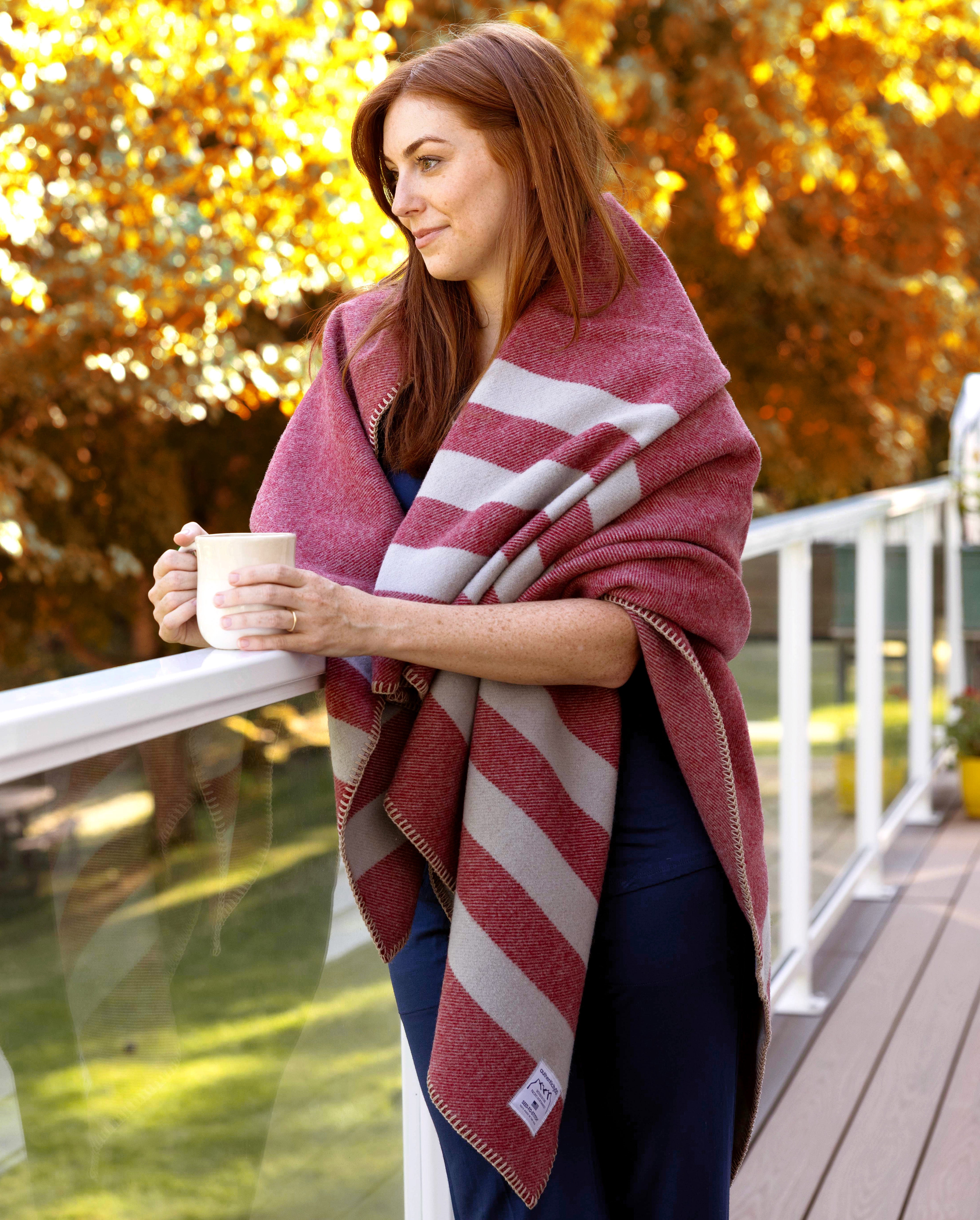 Woman enjoying the fall foliage on her back deck with a cup of coffee and a Northwest Wool throw draped on her shoulders.