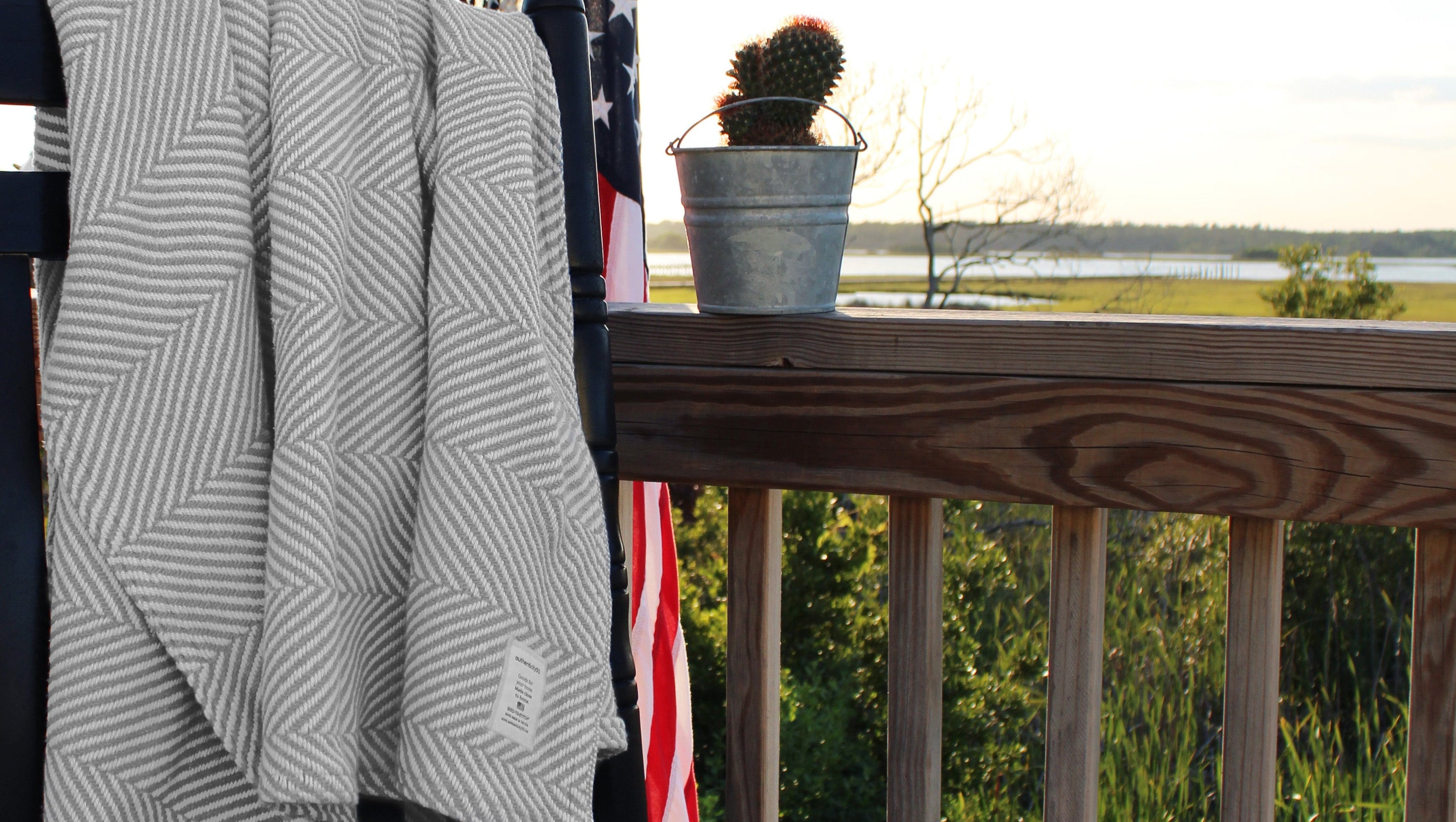 Cascade Gray Heritage Blanket draped on the back of a rocking chair with an American flag hanging in the background.