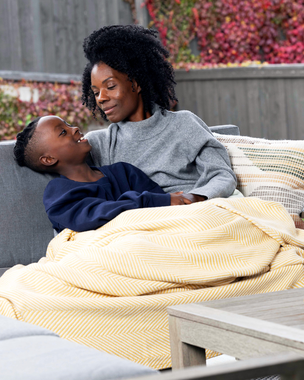 Mother and son sitting and smiling in their backyard with a Heritage Blanket on their laps.