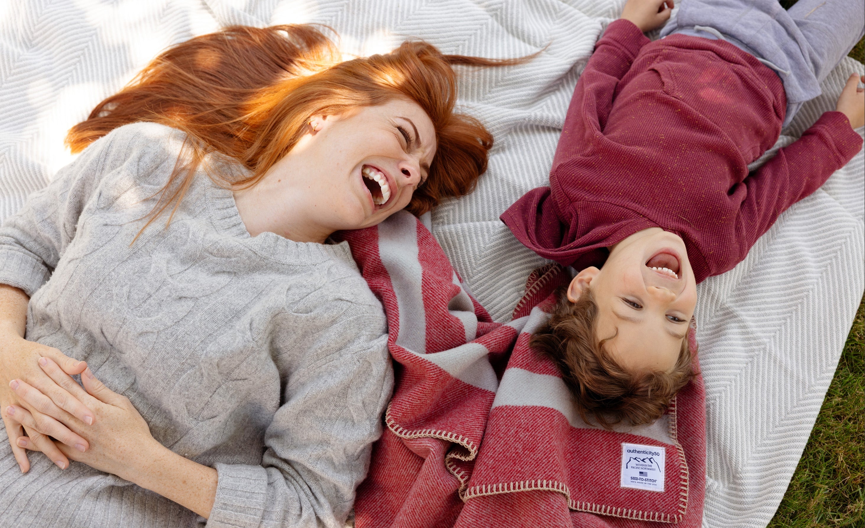 Mother and son laying in their backyard on their Northwest Wool Throw and Heritage Blanket.