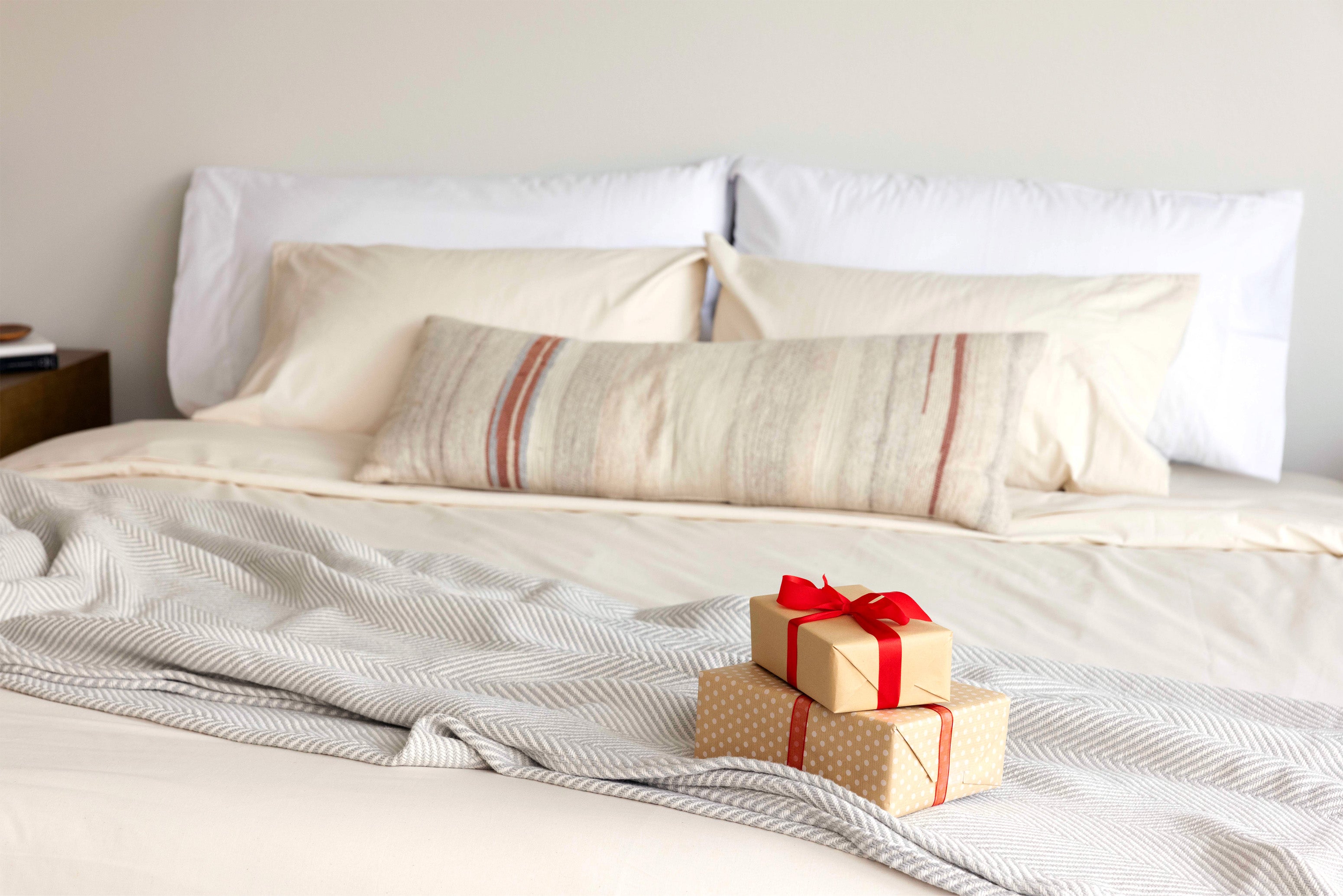Stack of wrapped gifts on a bed made with Authenticity50's Made in USA bedding and home goods.