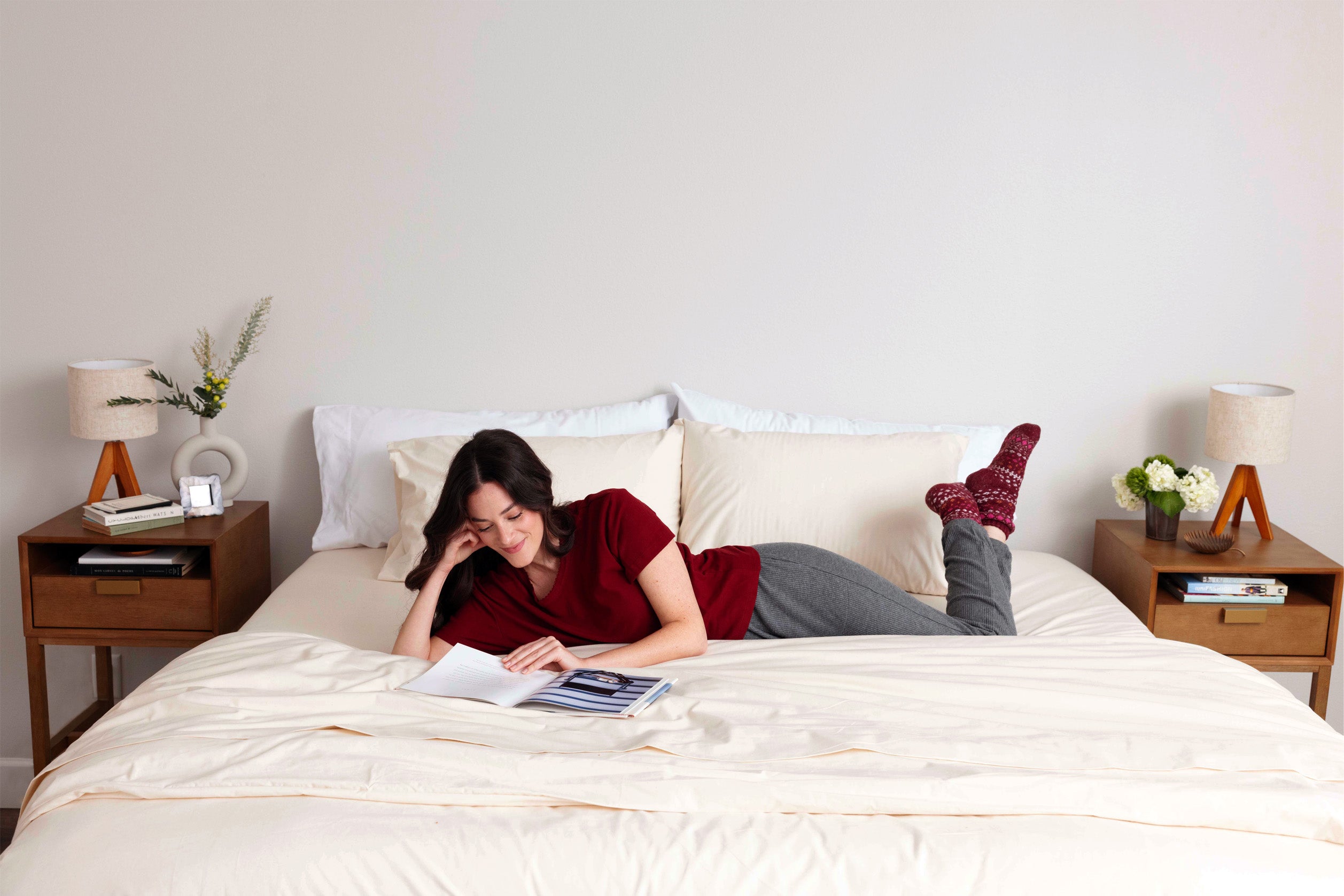 Woman laying in bed reading and smiling. The bed is dressed in Heritage American Sheets and an A50 Duvet Cover.