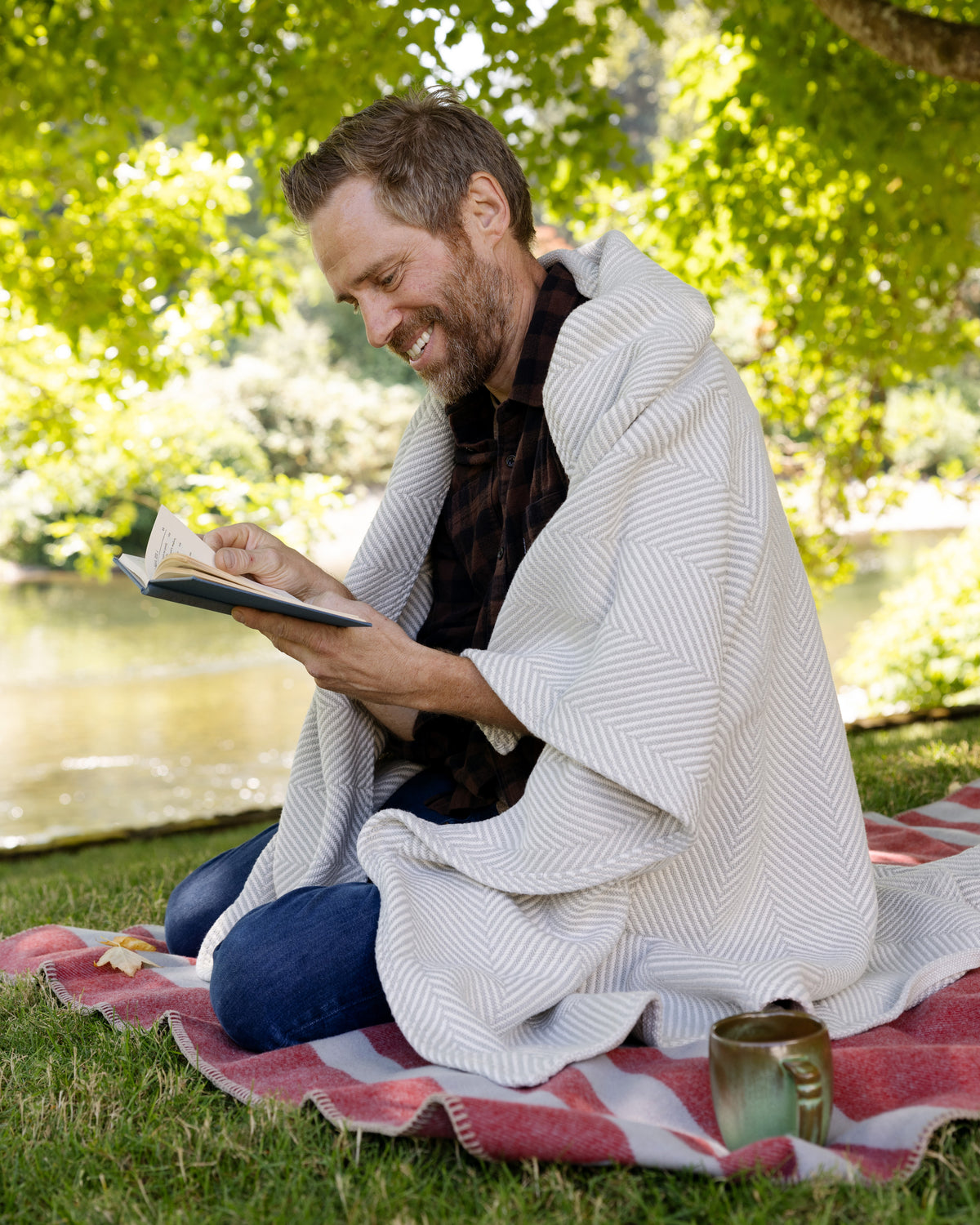 Man sitting in his backyard reading, wrapped in a Cascade Gray Heritage Blanket.