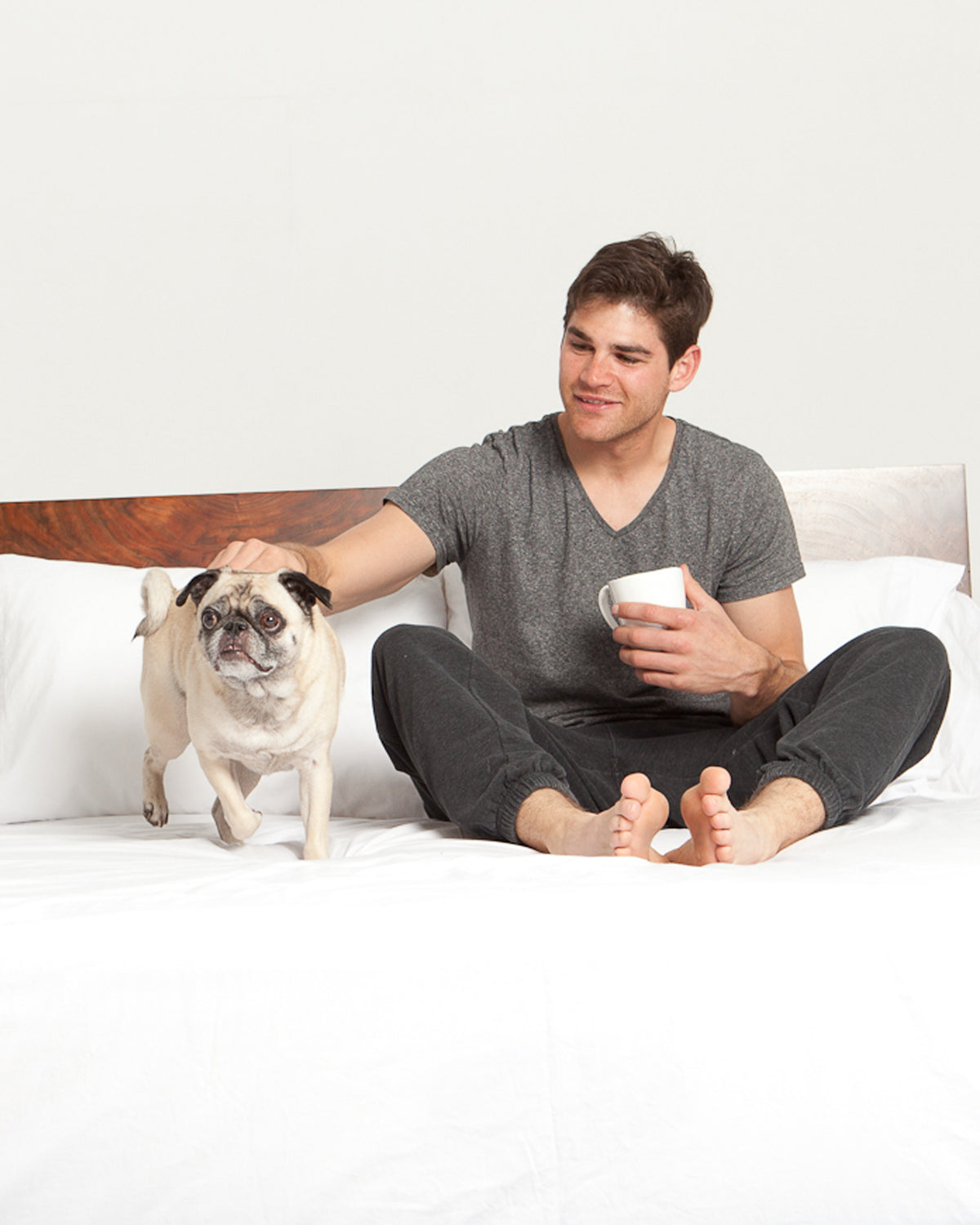 Man sitting in bed, made with Cloud White Heritage American Sheets, petting a dog.