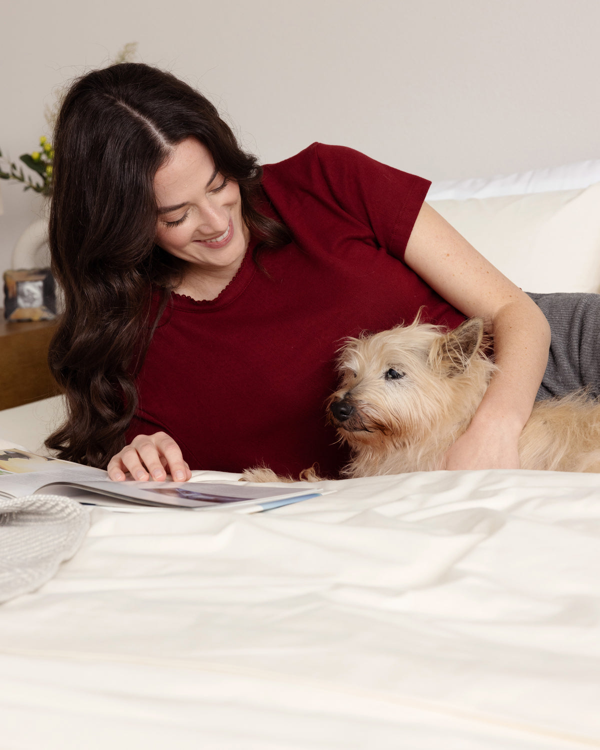 Woman reading in bed, made with Rustic Cotton Heritage American Sheets, snuggled up with her dog.