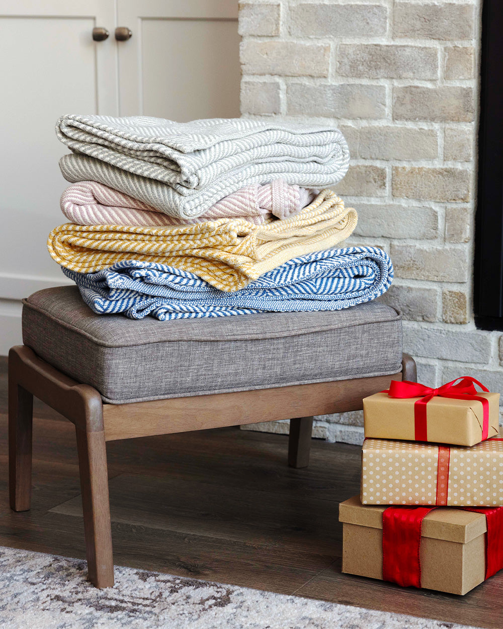 Stack of four Heritage Blankets sitting on a footstool with a stack of wrapped presents nearby.