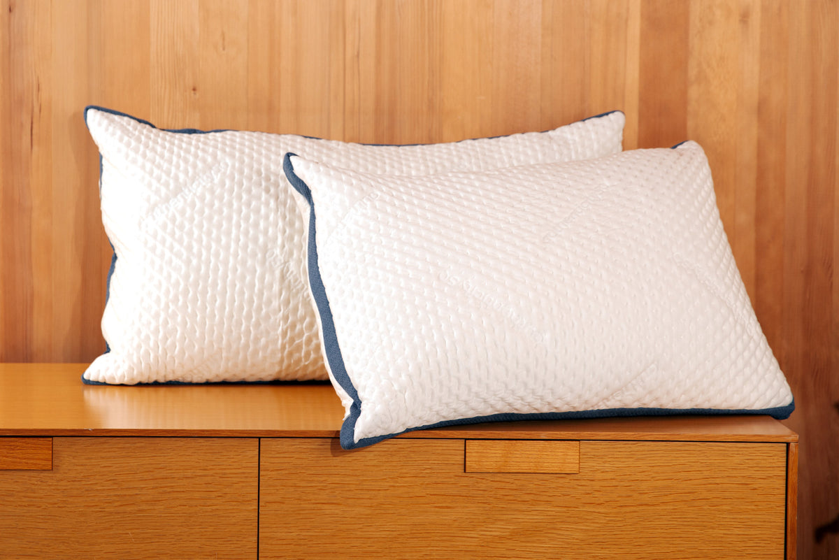 Two Custom Comfort Pillows resting on a table, propped up against a wood wall.