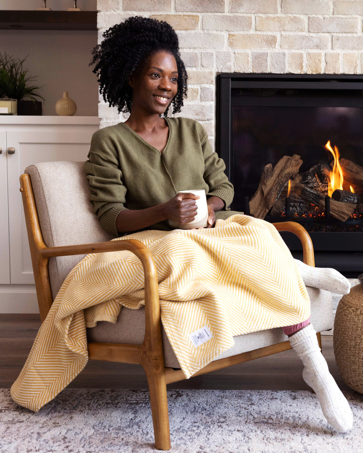 Woman sipping coffee by the fireplace with her Prairie Yellow Heritage Blanket.
